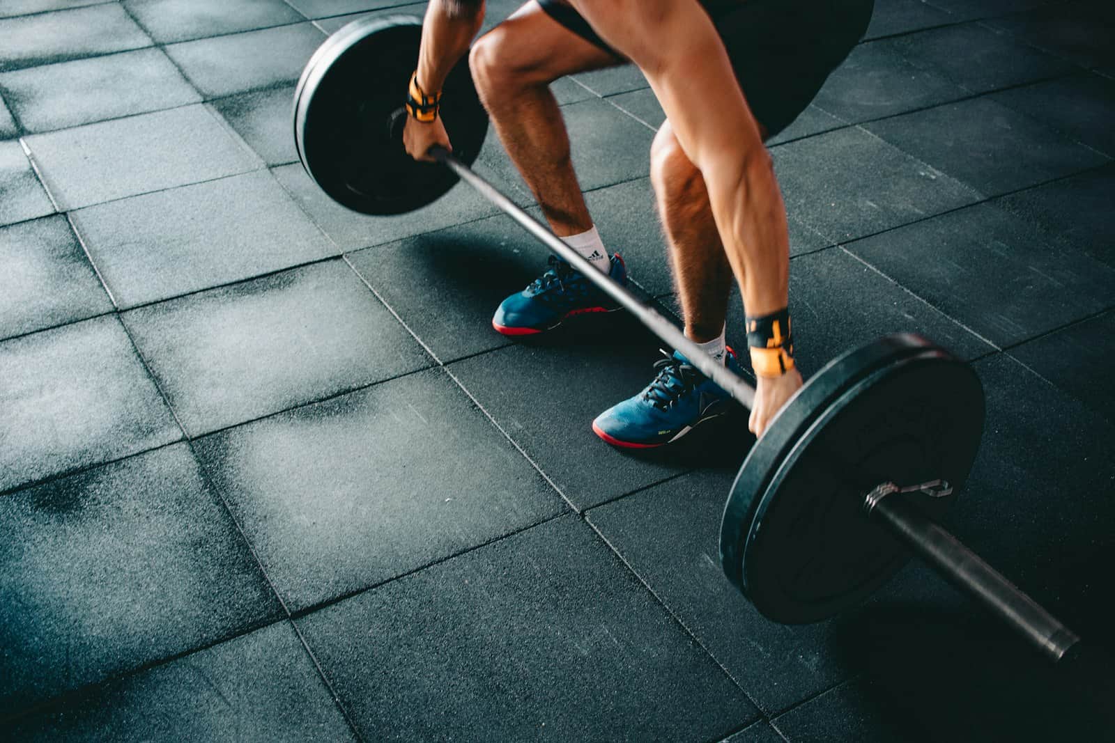 Lifter setting up a barbell deadlift on dark rubber gym flooring, hands finding grip