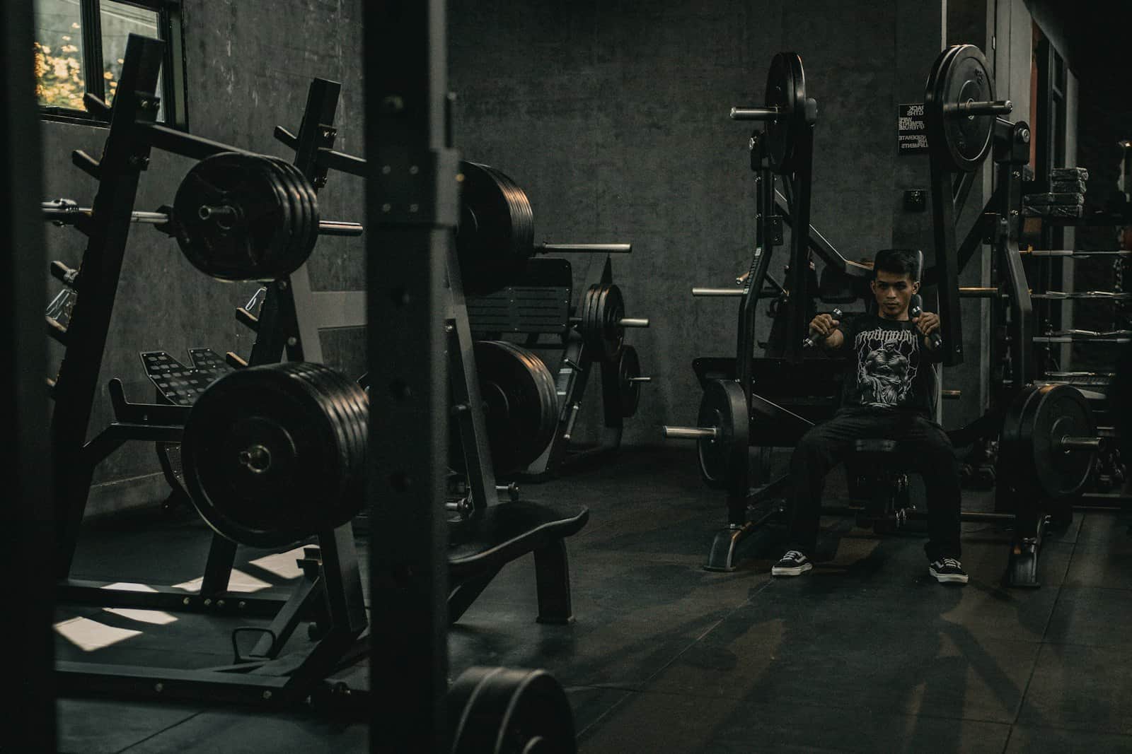 Member sitting on a bench between sets in a dark gym, racks of plates behind him