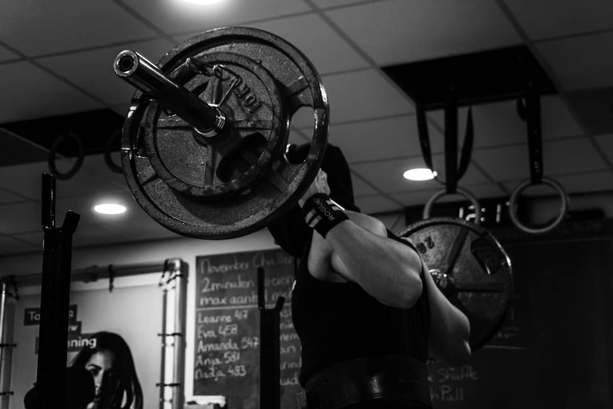 Coach Dre racking a heavy clean during his own training, programming whiteboard behind him, black and white