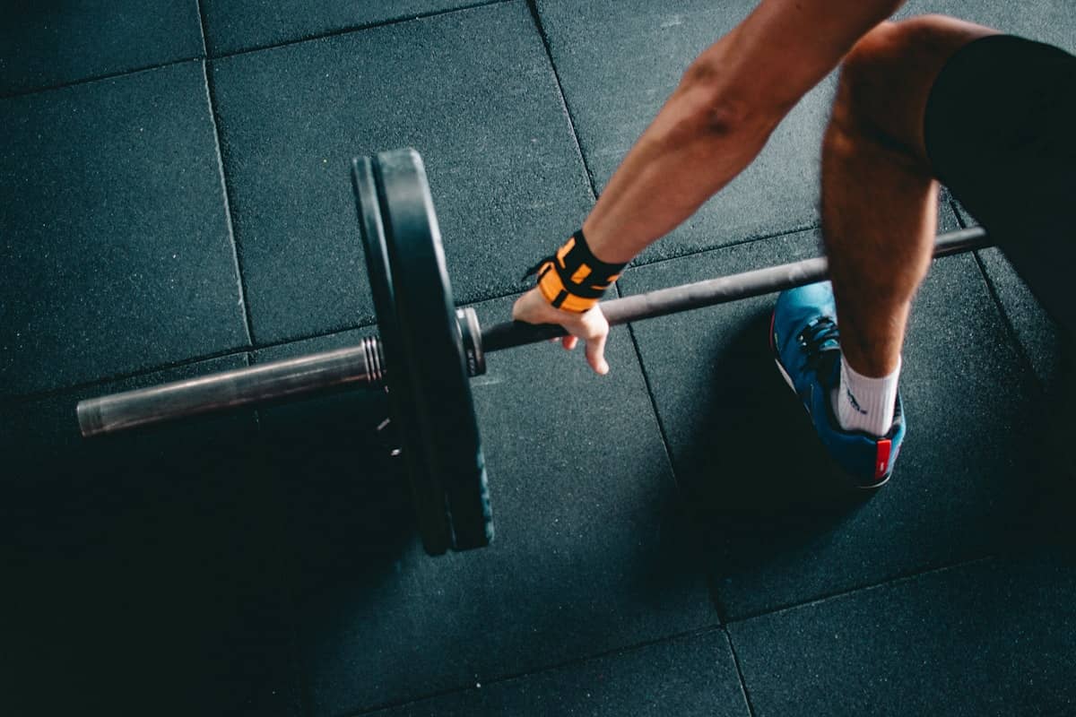 Overhead view of a lifter's straps and grip on a barbell over dark flooring