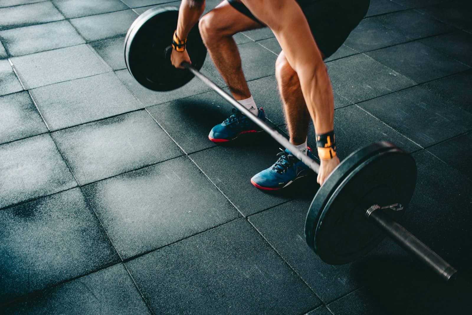 Lifter setting up a barbell deadlift on dark rubber gym flooring, hands finding grip