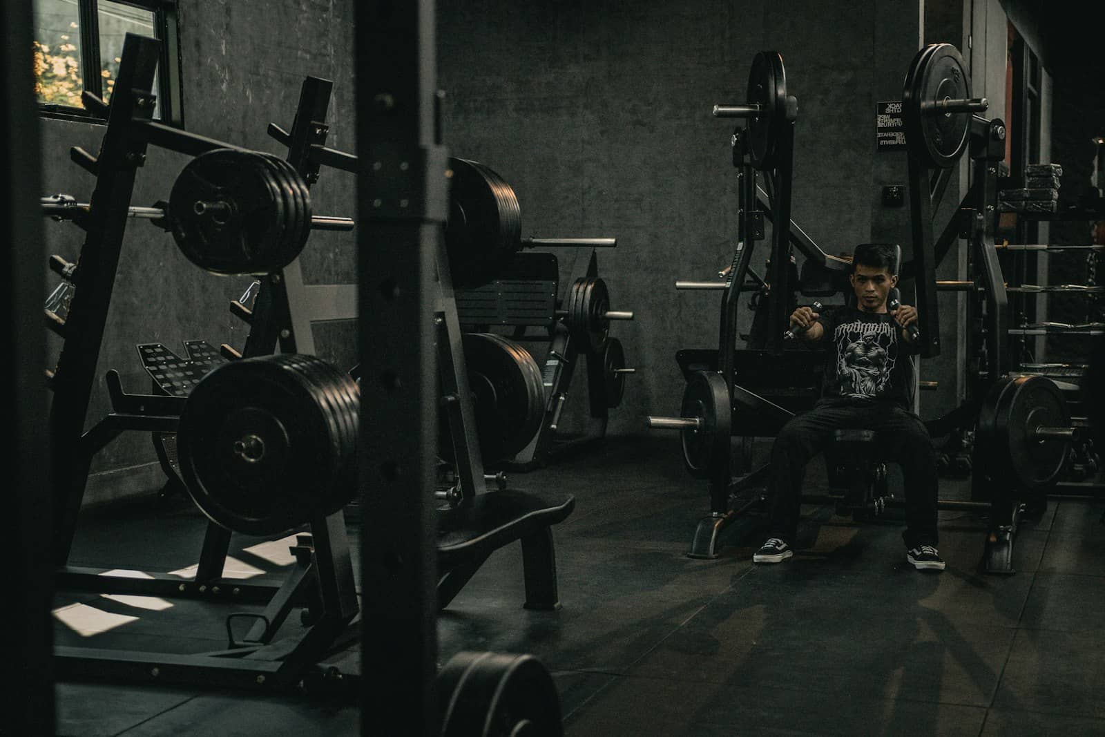 Member sitting on a bench between sets in a dark gym, racks of plates behind him