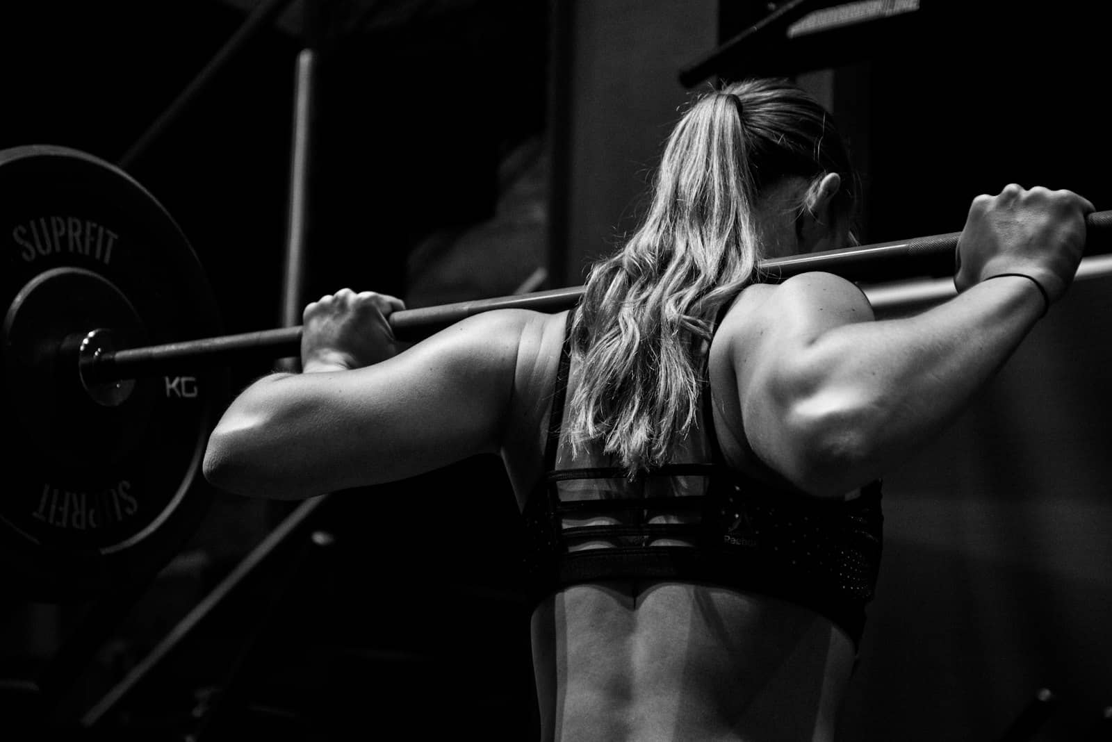 Athlete under a loaded barbell back squat, coach's-eye view from behind, black and white
