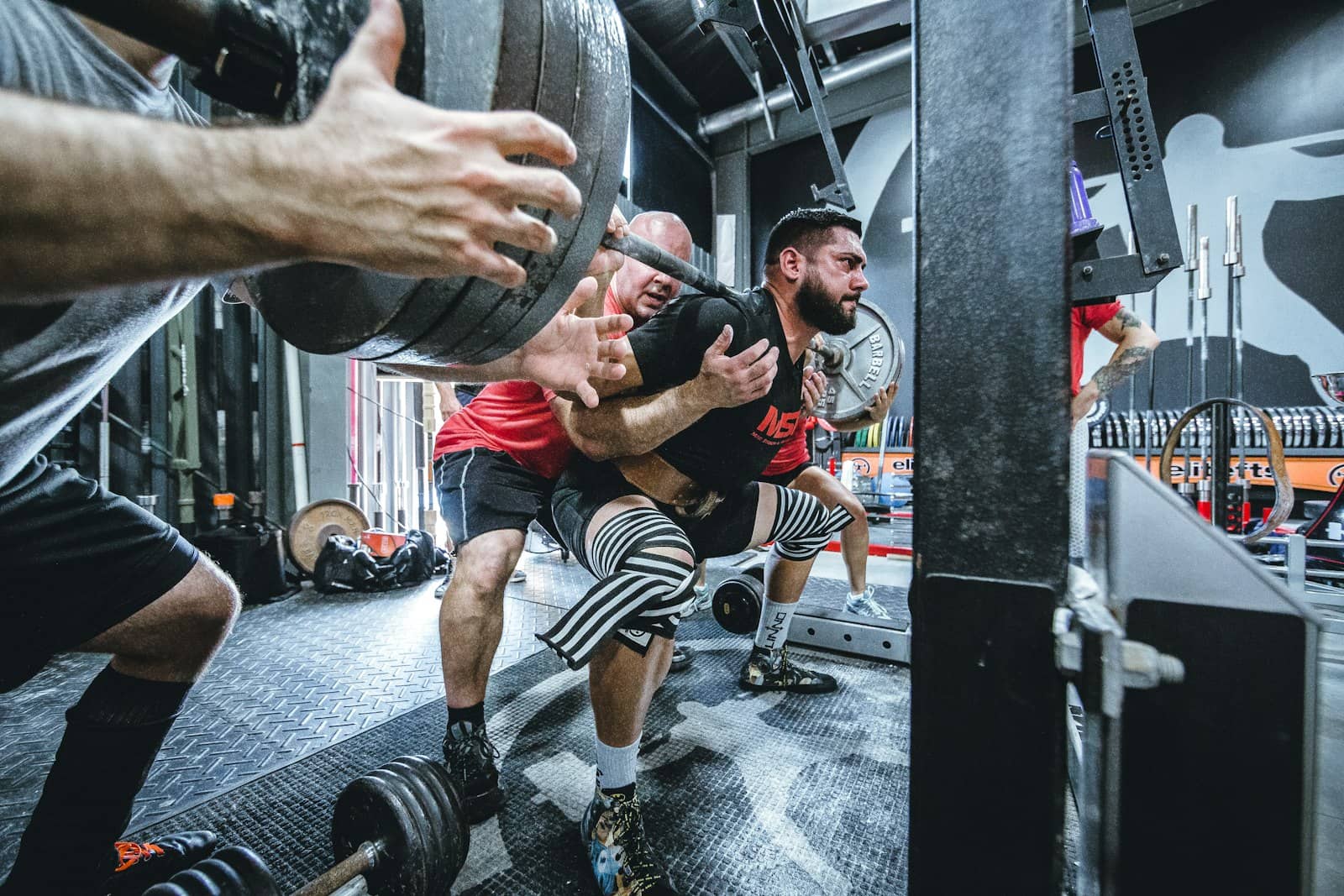 Small group of lifters spotting a heavy barbell back squat in a training gym