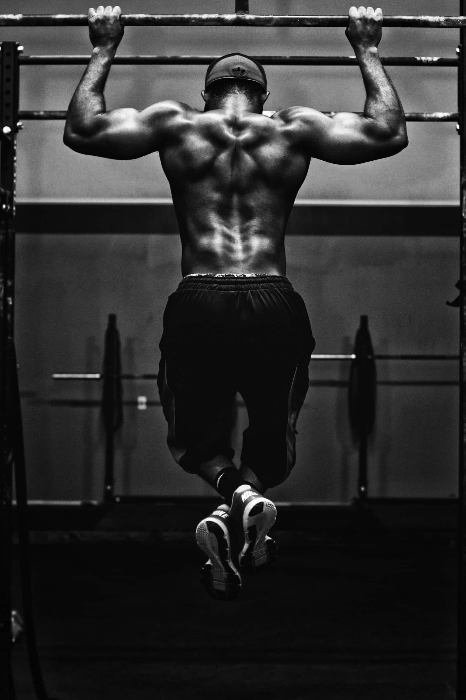 Lifter at the top of a strict pull-up on a gym rig, photographed in black and white