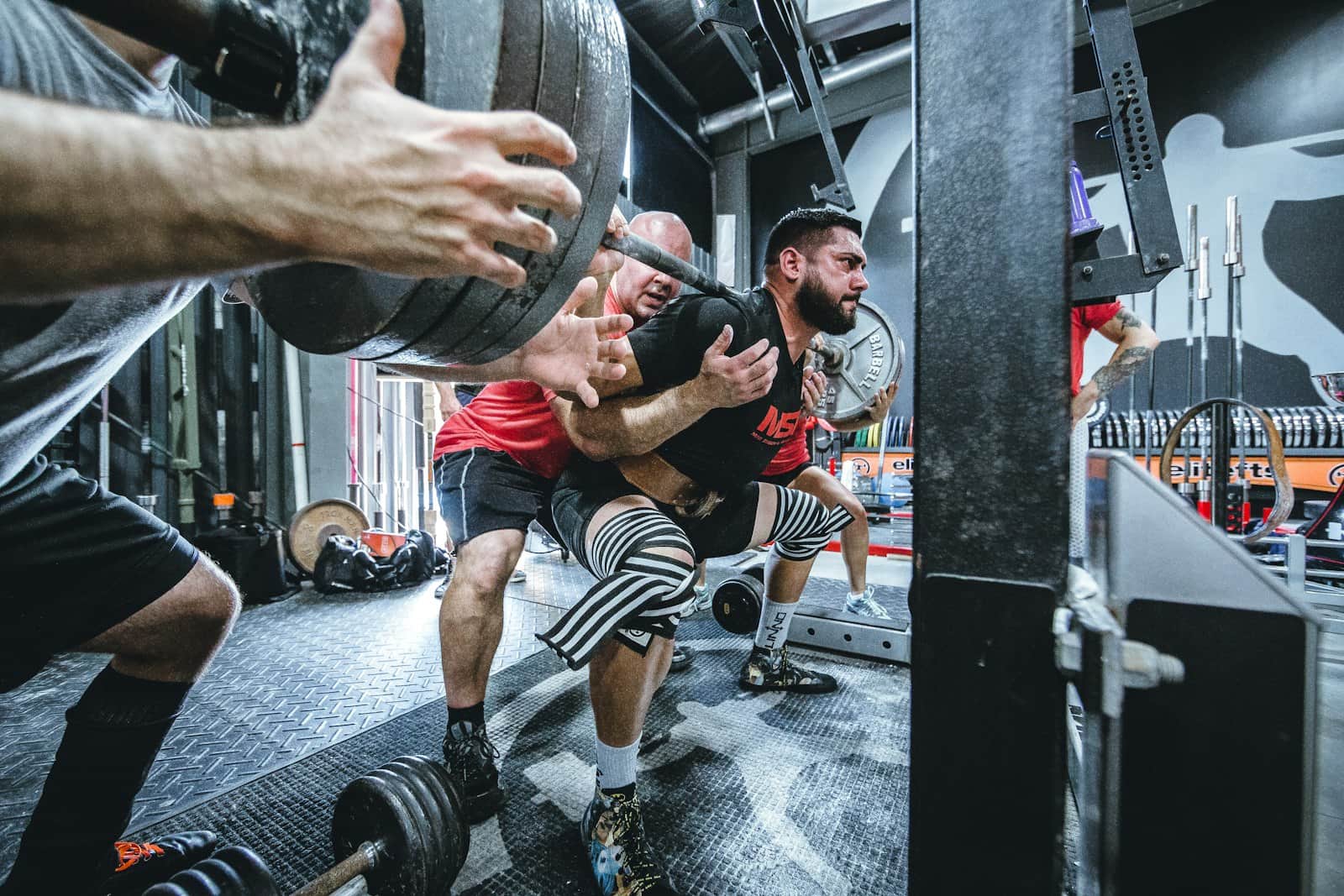 Small group of lifters spotting a heavy barbell back squat in a training gym